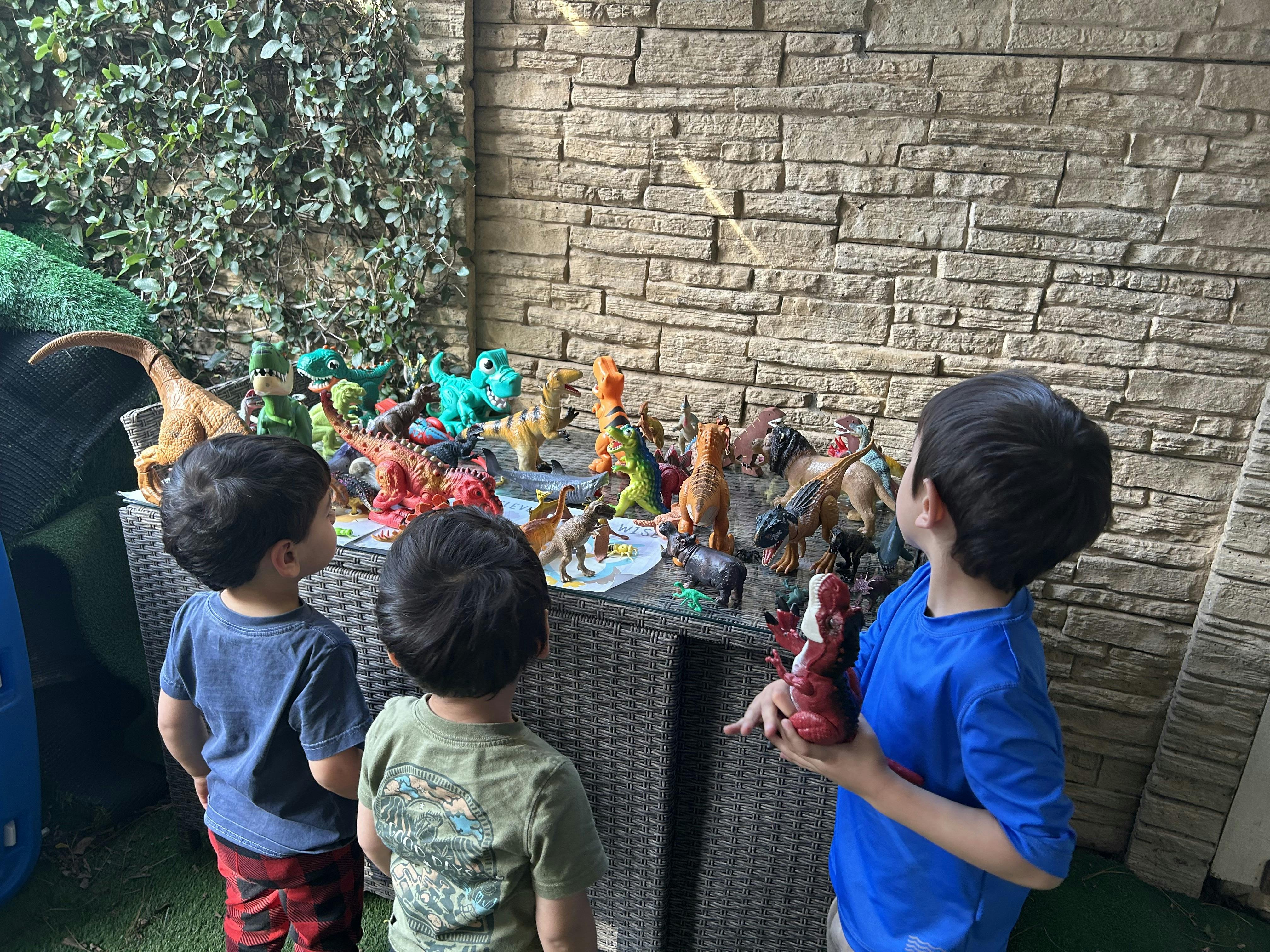 Three children looking at a table full of dinosaur toys