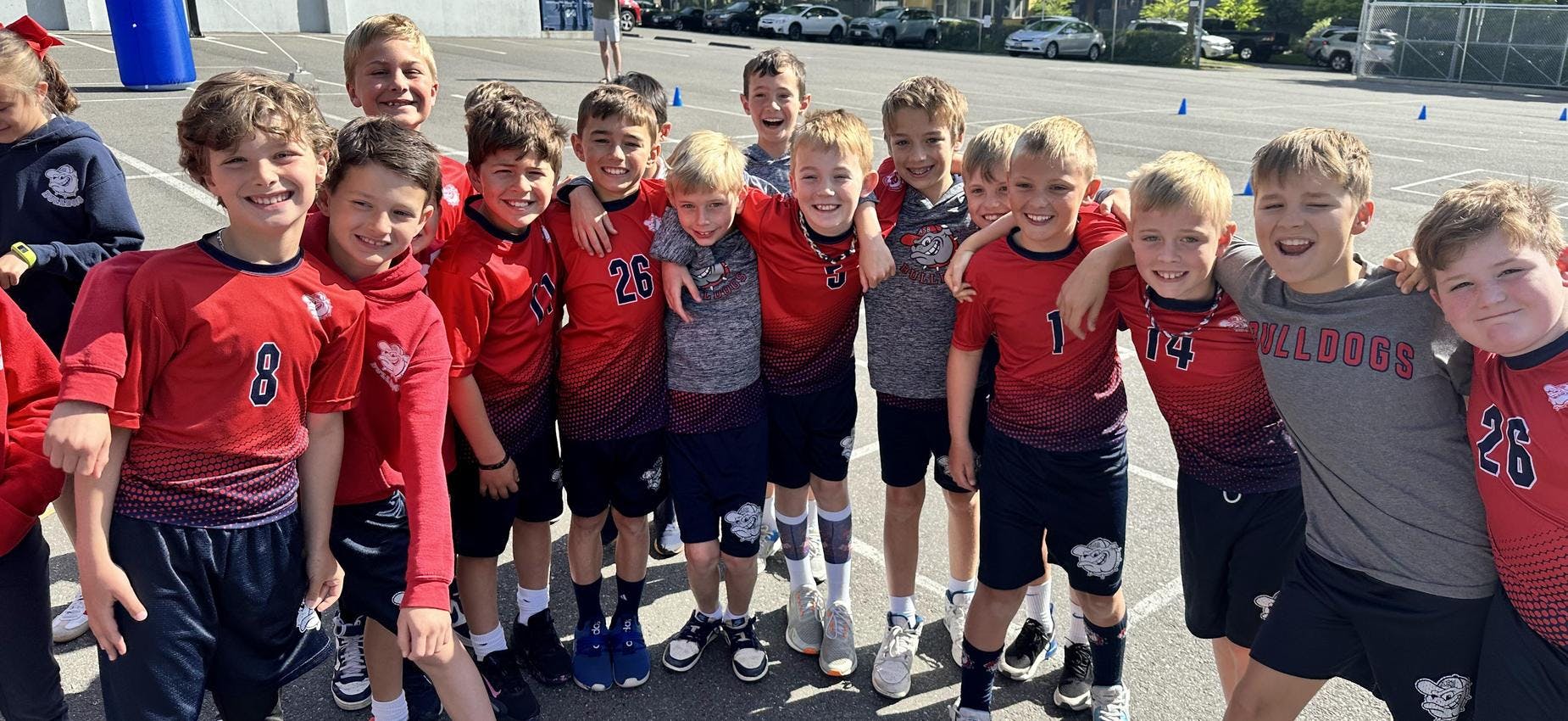 Group of children in athletic wear, some in red jerseys, smiling at the camera