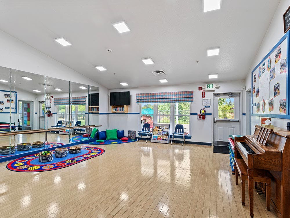 An empty children's activity room with a large mirror wall and a piano
