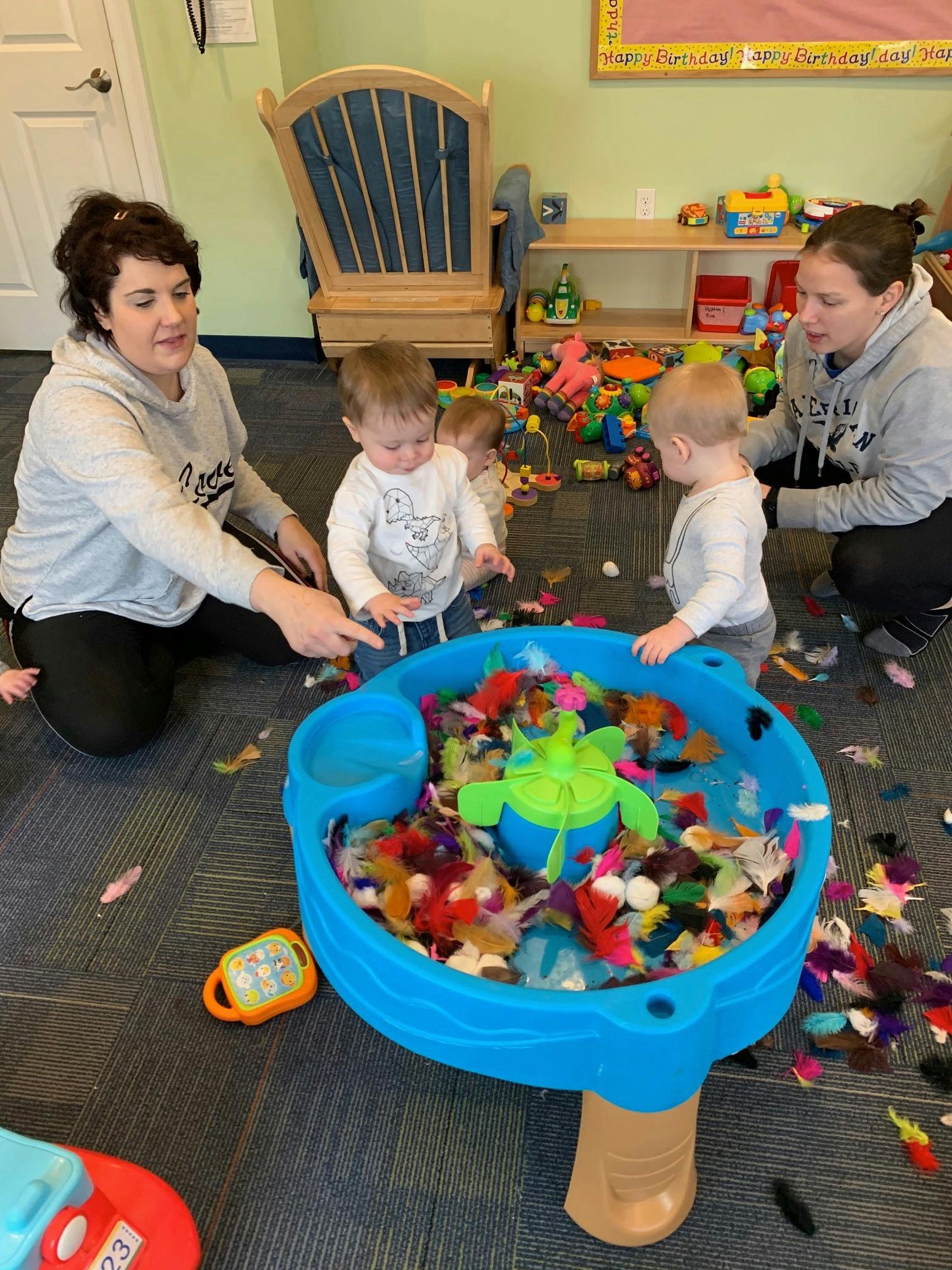 Two people and three children playing around a blue sensory table
