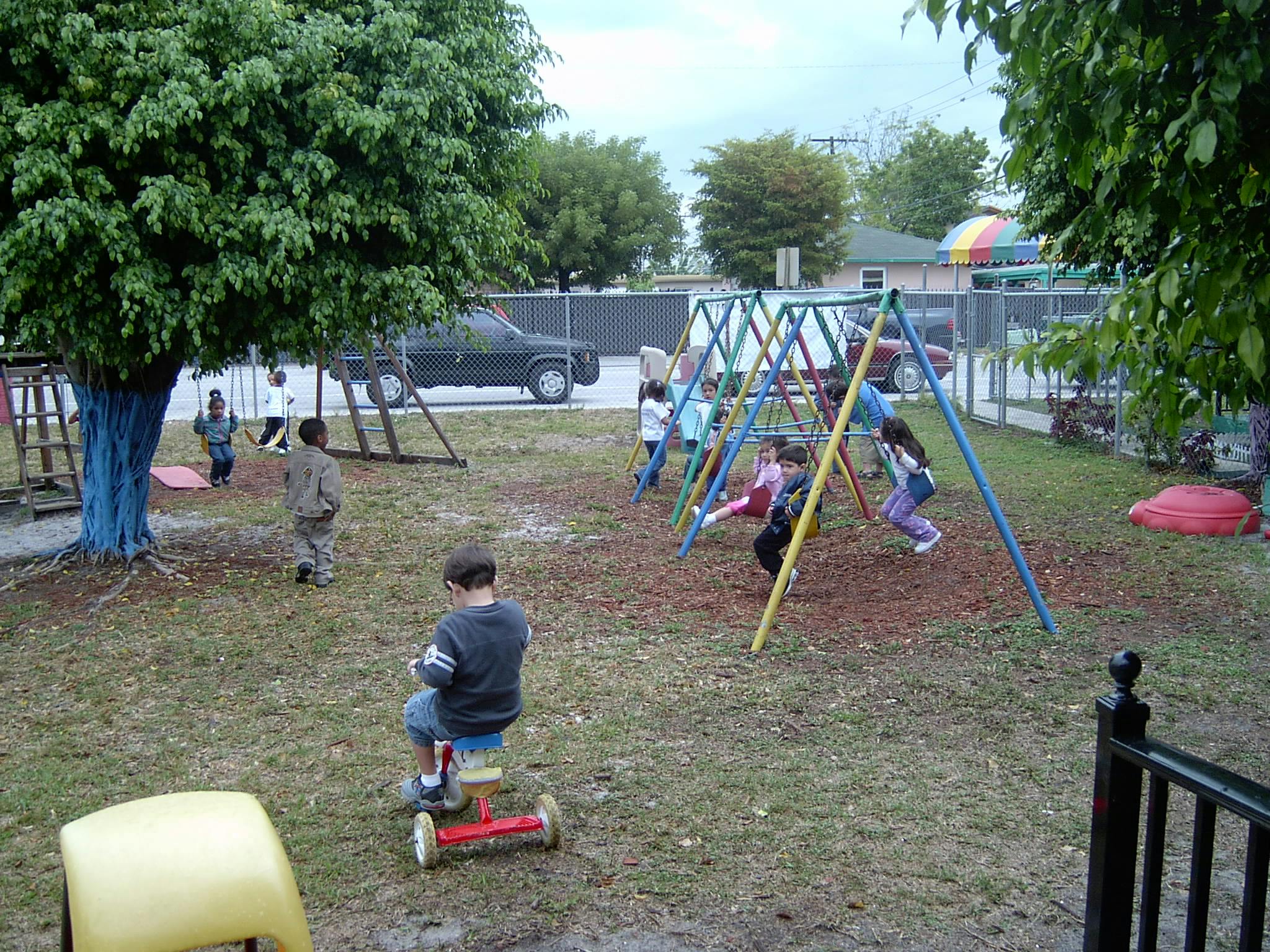 Children playing on a swing set and riding a toy in a grassy area