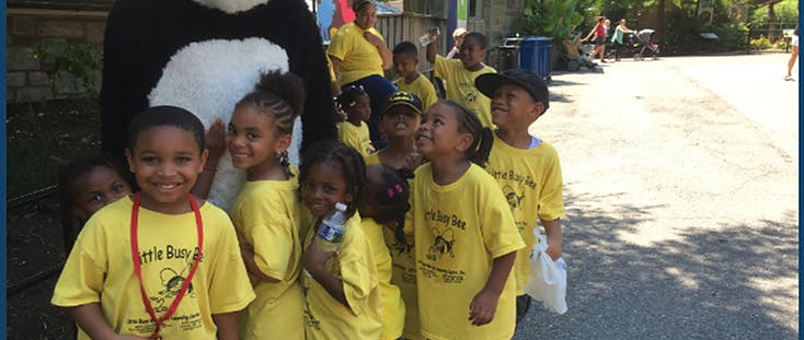 Group of children in yellow shirts standing near a person in a panda costume
