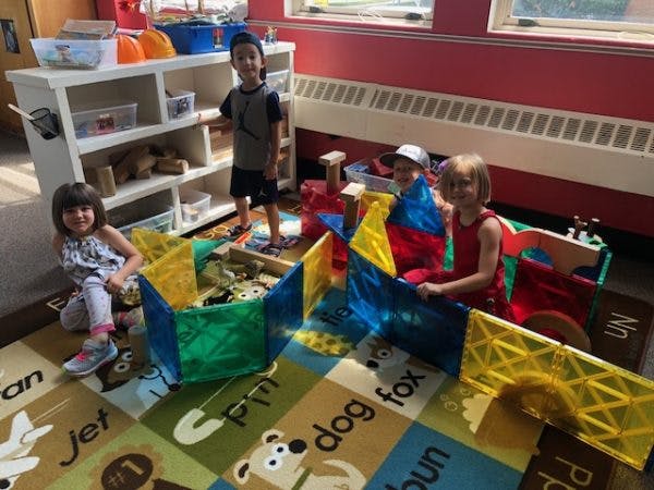 Three children playing with colorful building blocks in a classroom