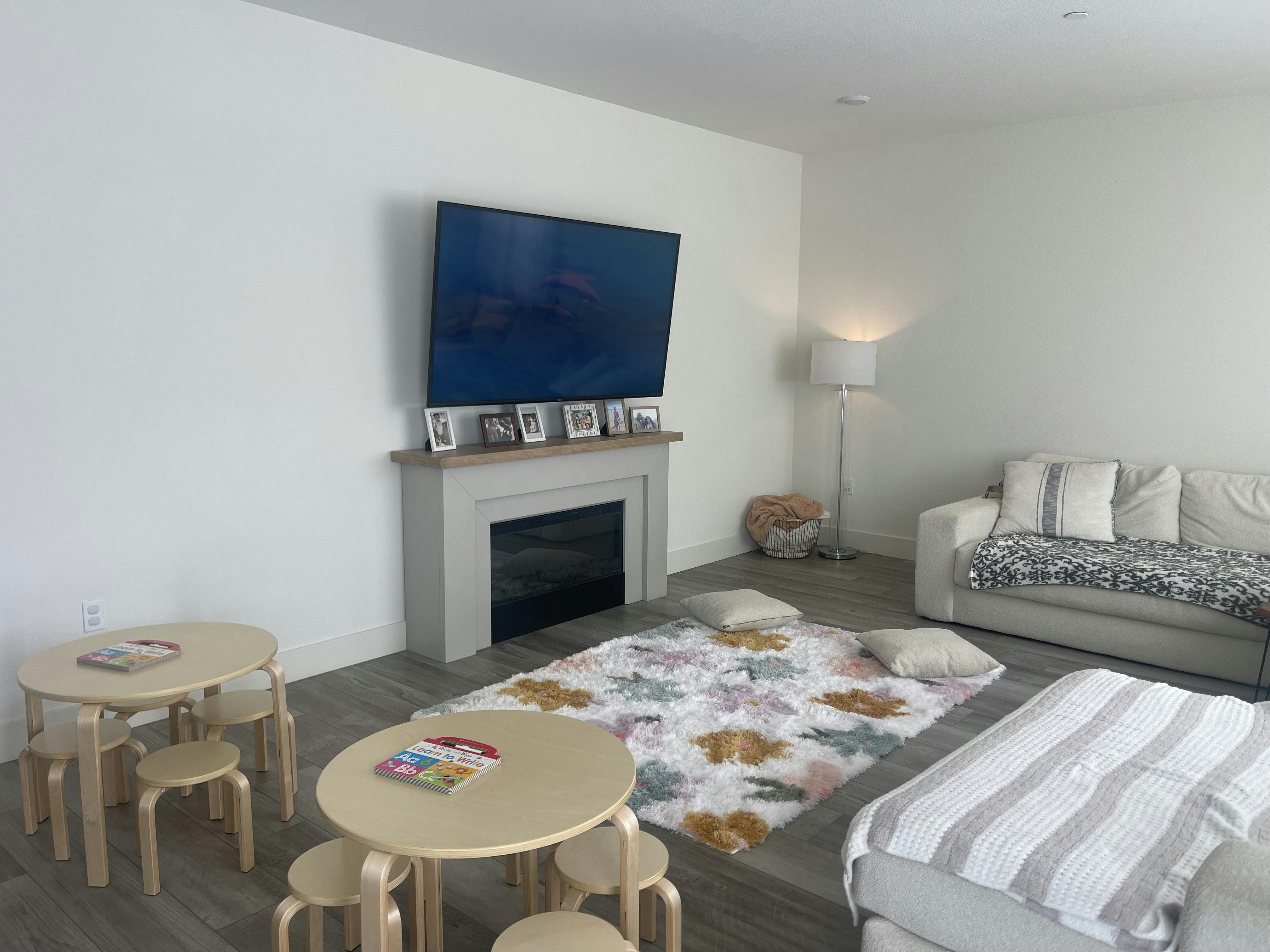 Living room with television above a fireplace and small round tables for children