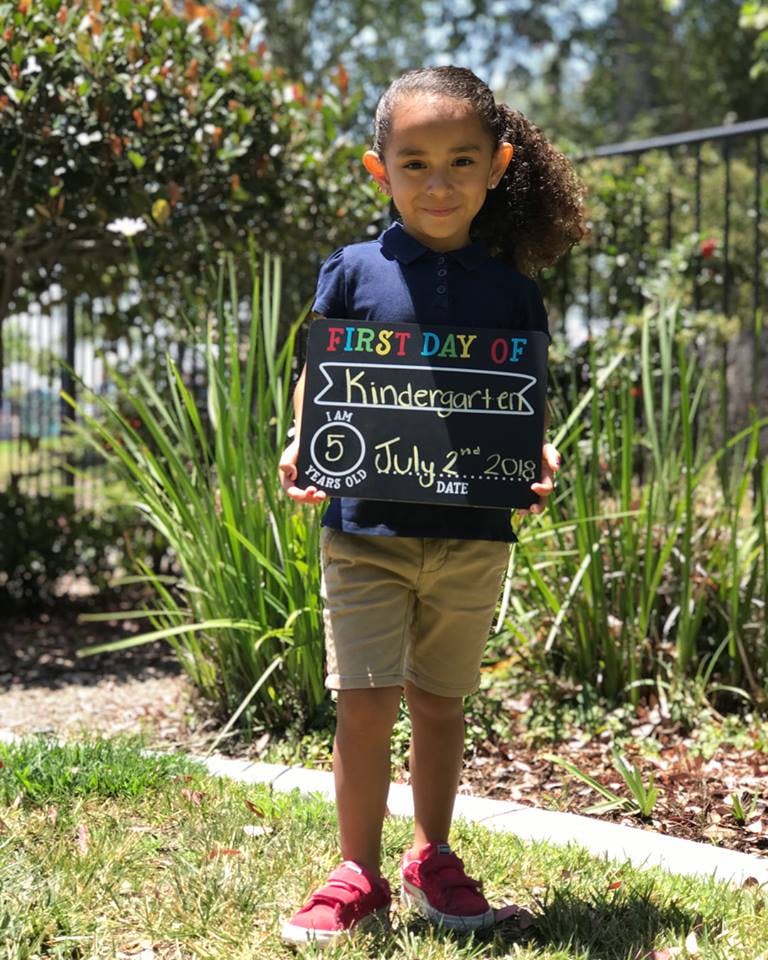 Child holding a chalkboard sign that reads "First Day of Kindergarten"