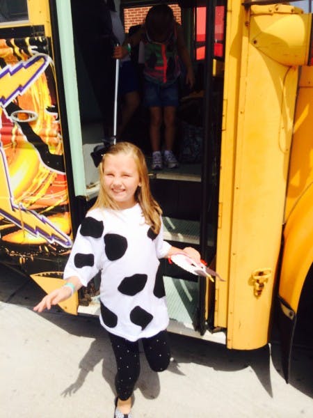 Child in a cow-print shirt standing in front of a school bus
