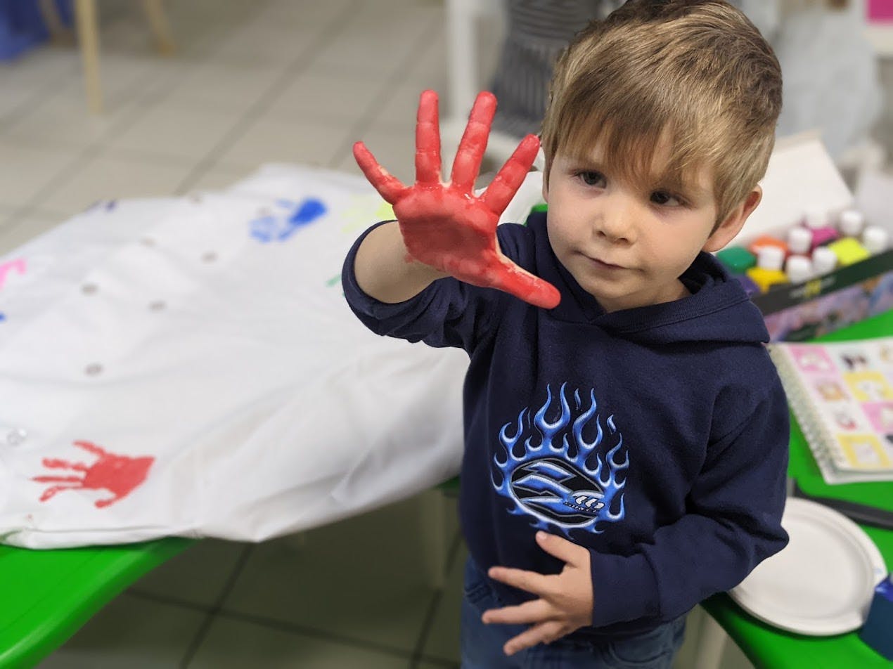 Child with red paint on one hand, holding it up