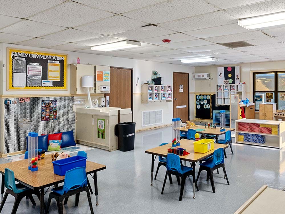 Classroom with small tables and chairs, shelves, and a bulletin board