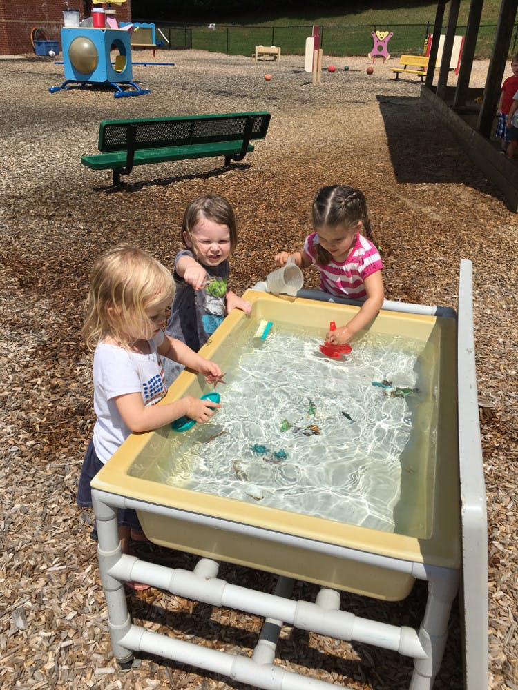 Three children playing with toys in a water table on a playground