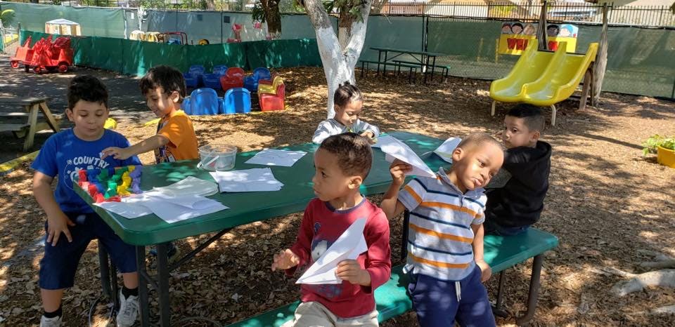 Children sitting at a picnic table with papers and art supplies
