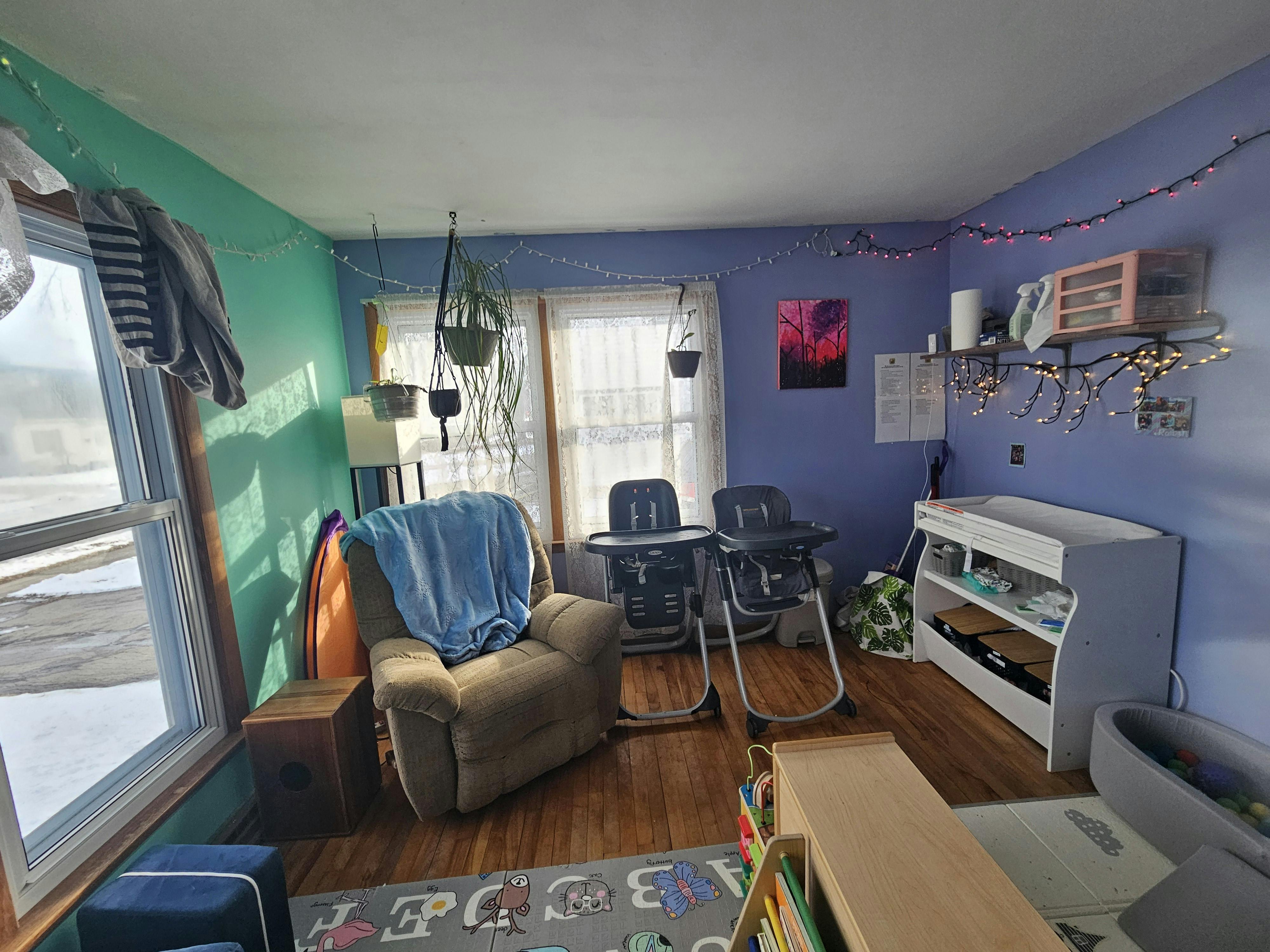 Living room with purple and teal walls, recliner, two high chairs, and changing table