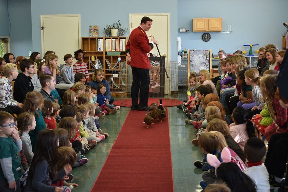 Person in red jacket on red carpet with children watching