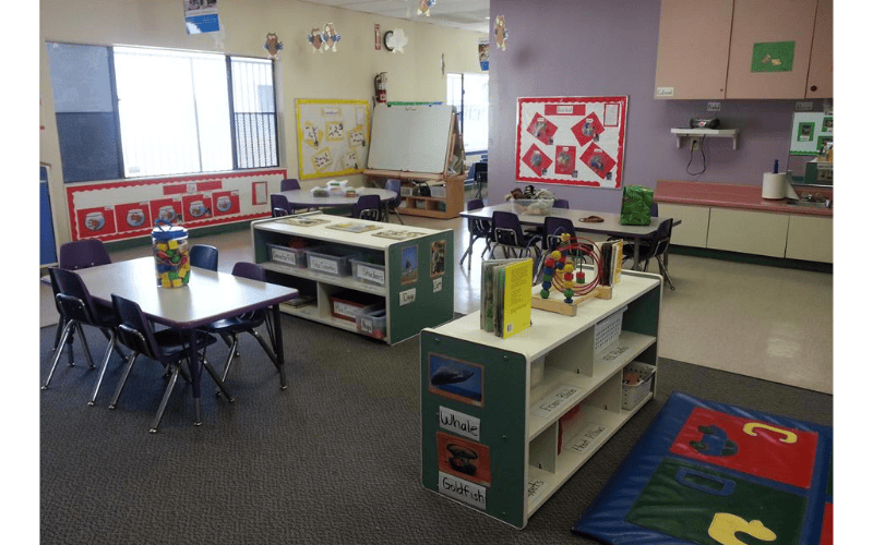 Classroom with small tables and chairs, shelves with toys, and posters on walls