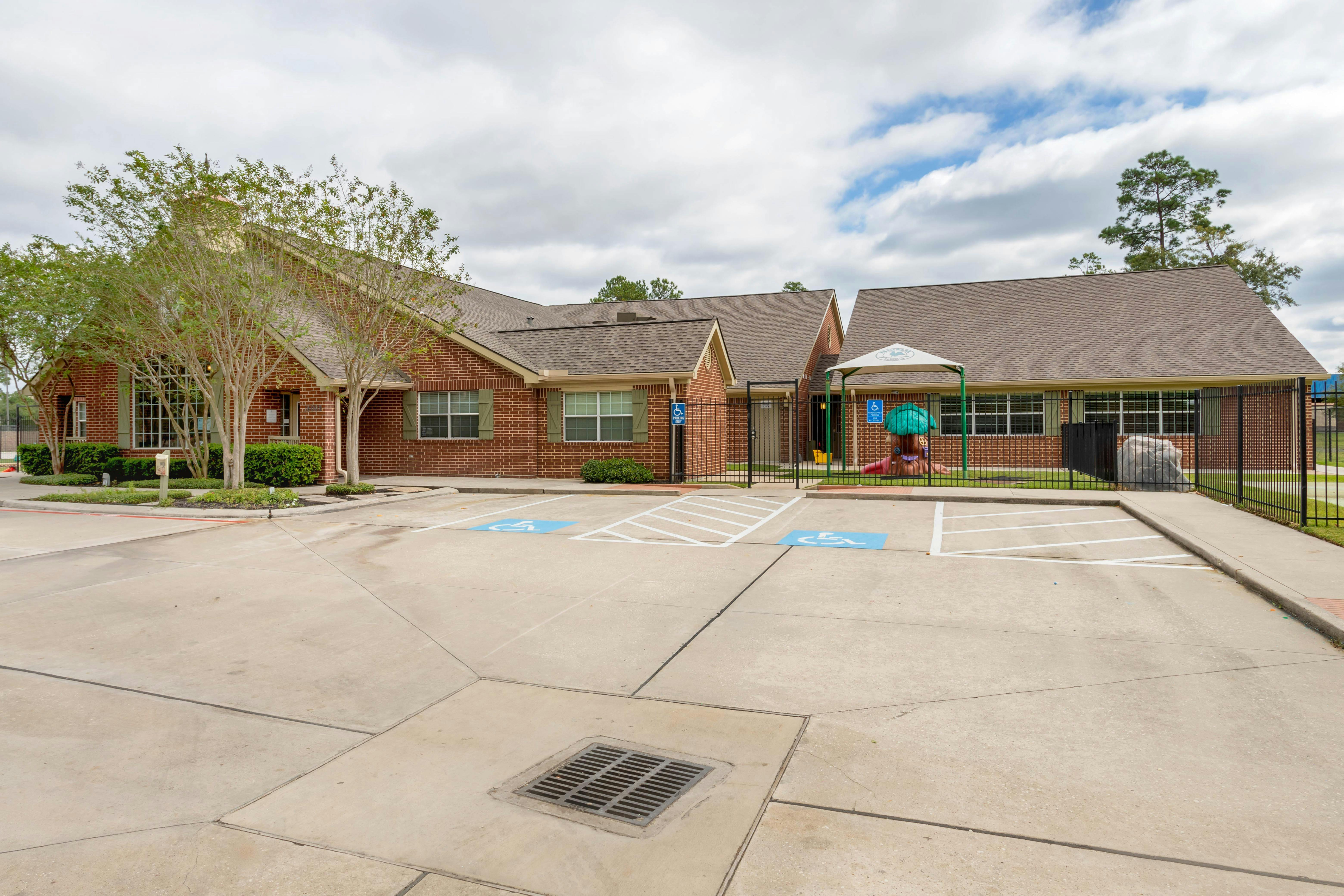 Brick building with green shutters, a parking lot, and a small playground with a shade