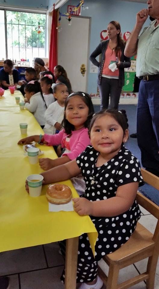 Children sitting at a table with a yellow tablecloth, one child with a donut
