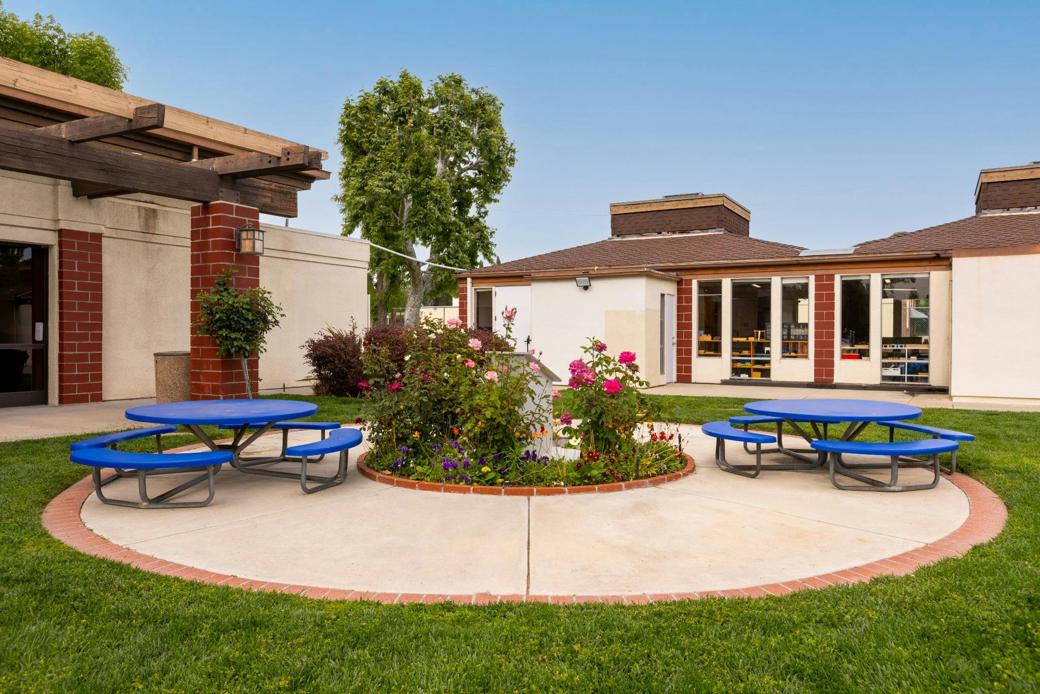 Outdoor area with two blue picnic tables on a concrete path with a garden