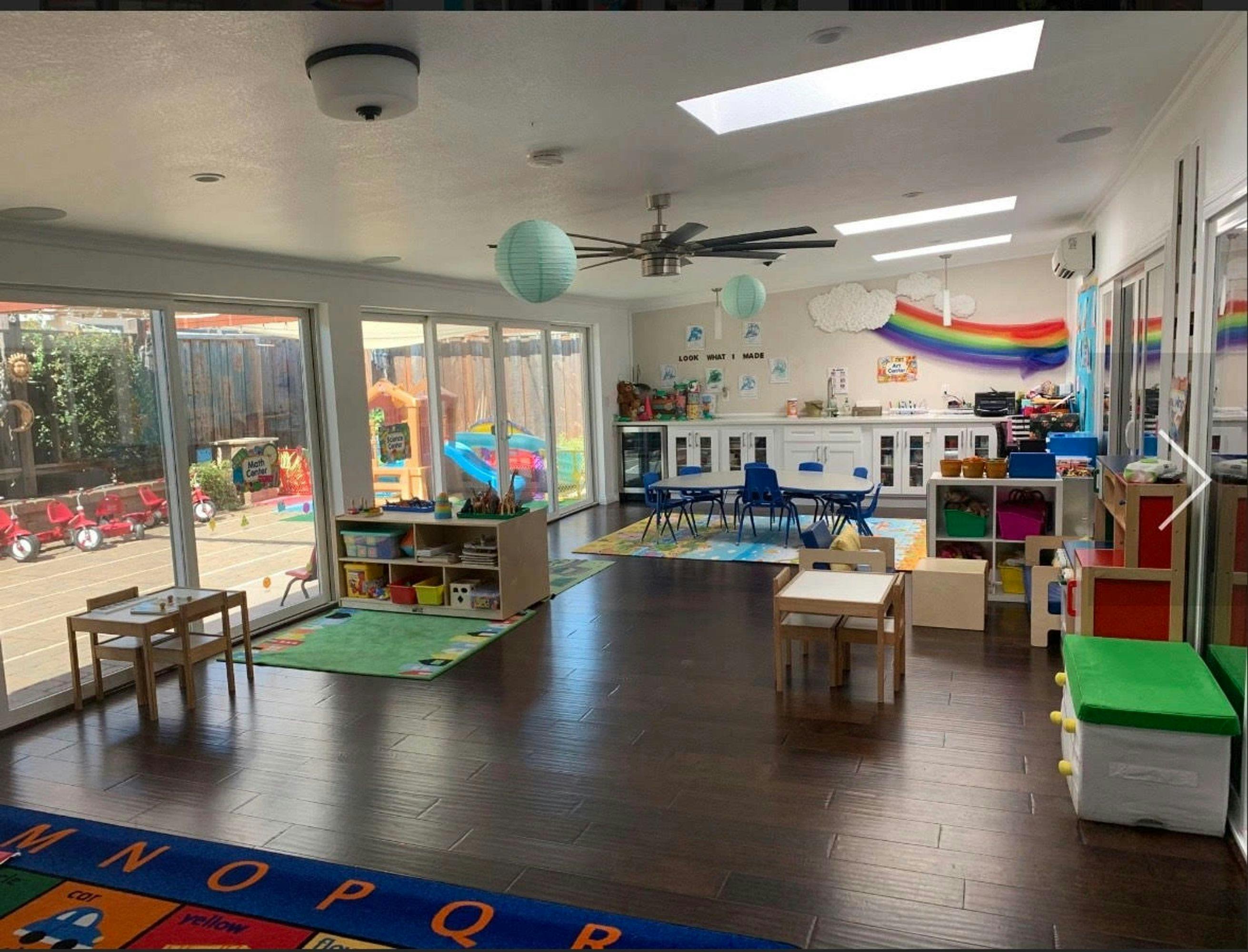 Classroom with tables, chairs, and toys, with a view of an outdoor play area