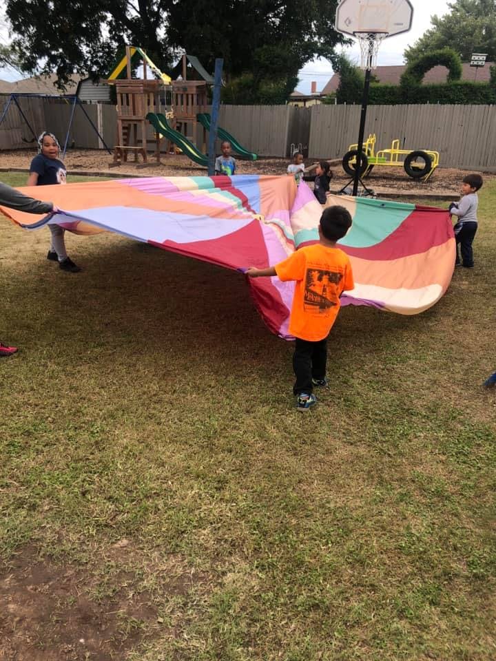 Children playing with a large colorful parachute on a grassy area