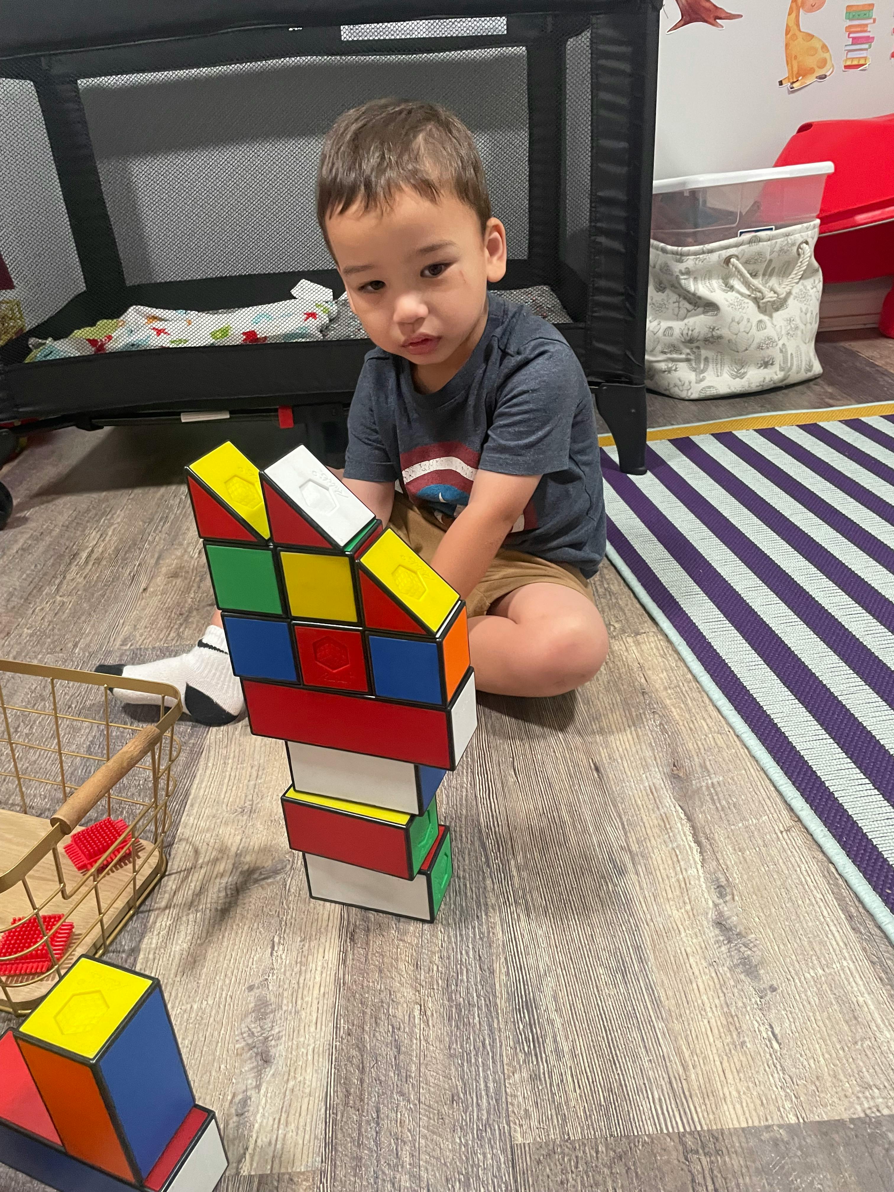 Child sitting on floor next to a tall structure made of colorful blocks