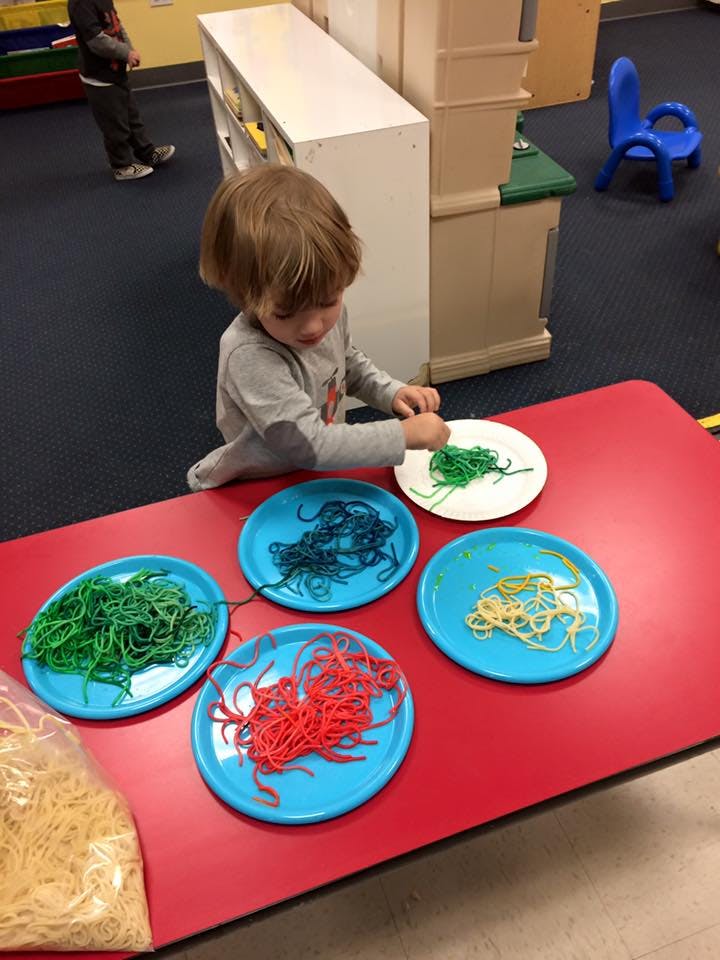 Child playing with colorful string on plates at a red table