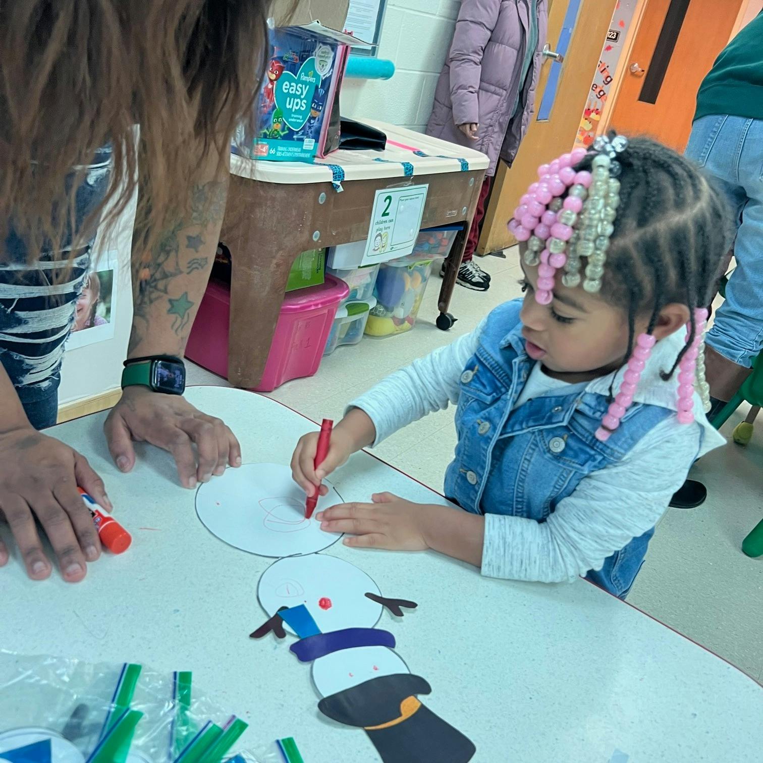 Child drawing on paper with a person in a classroom