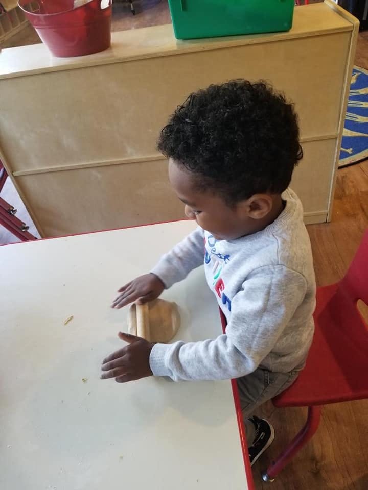 Child at a table rolling dough with a rolling pin