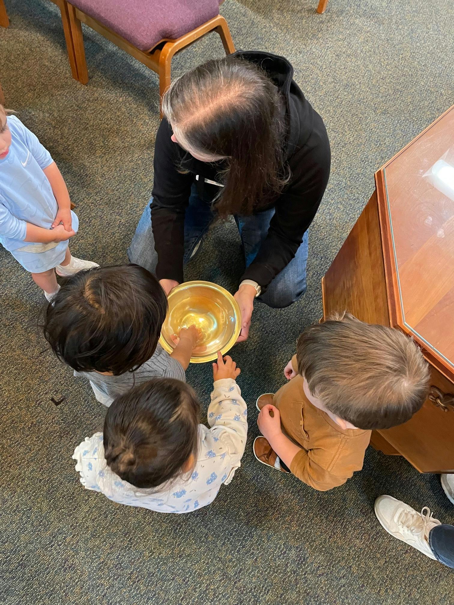 Person kneeling and holding a bowl as children gather around it