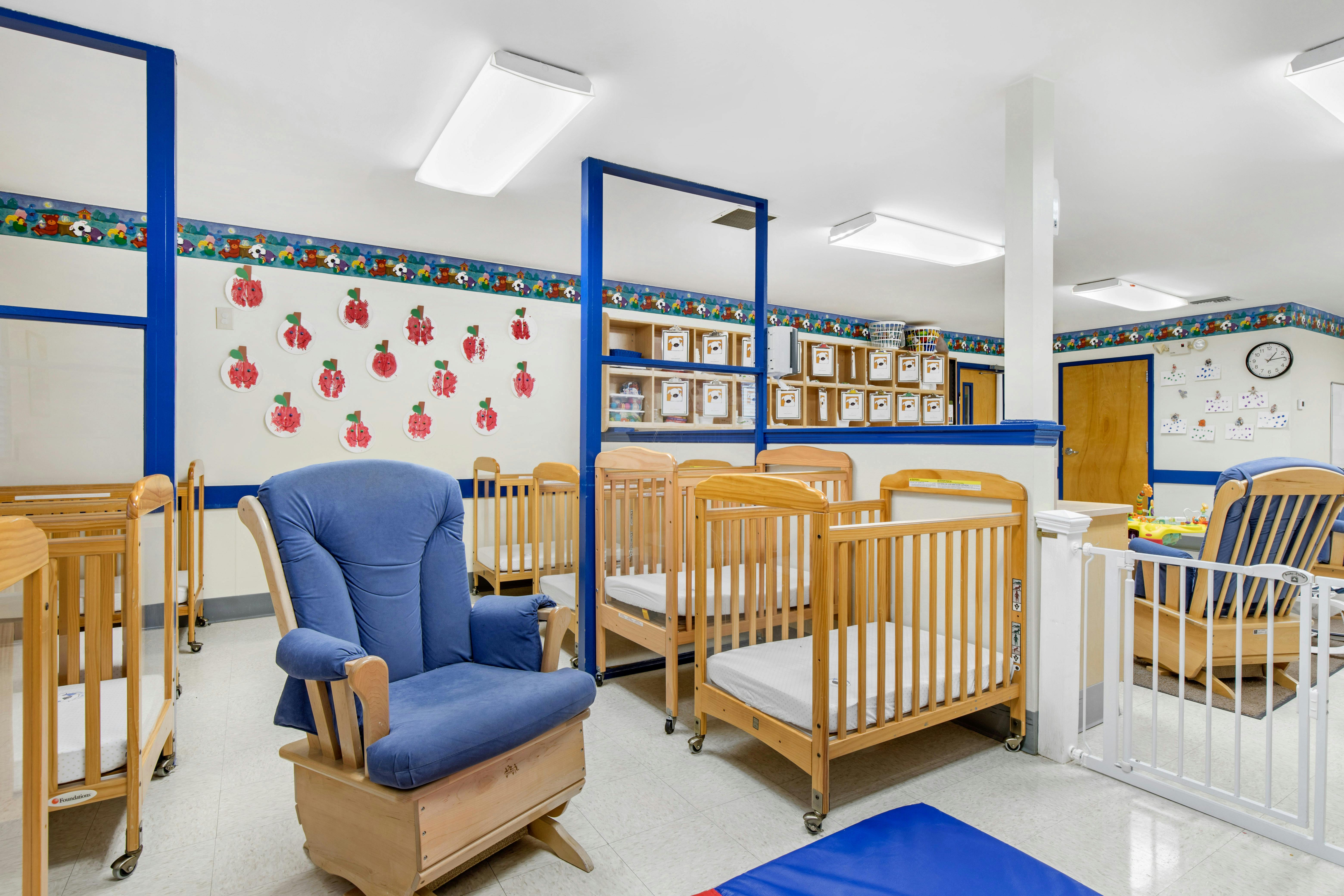 Baby room with several cribs, a blue rocking chair, and child art on the walls