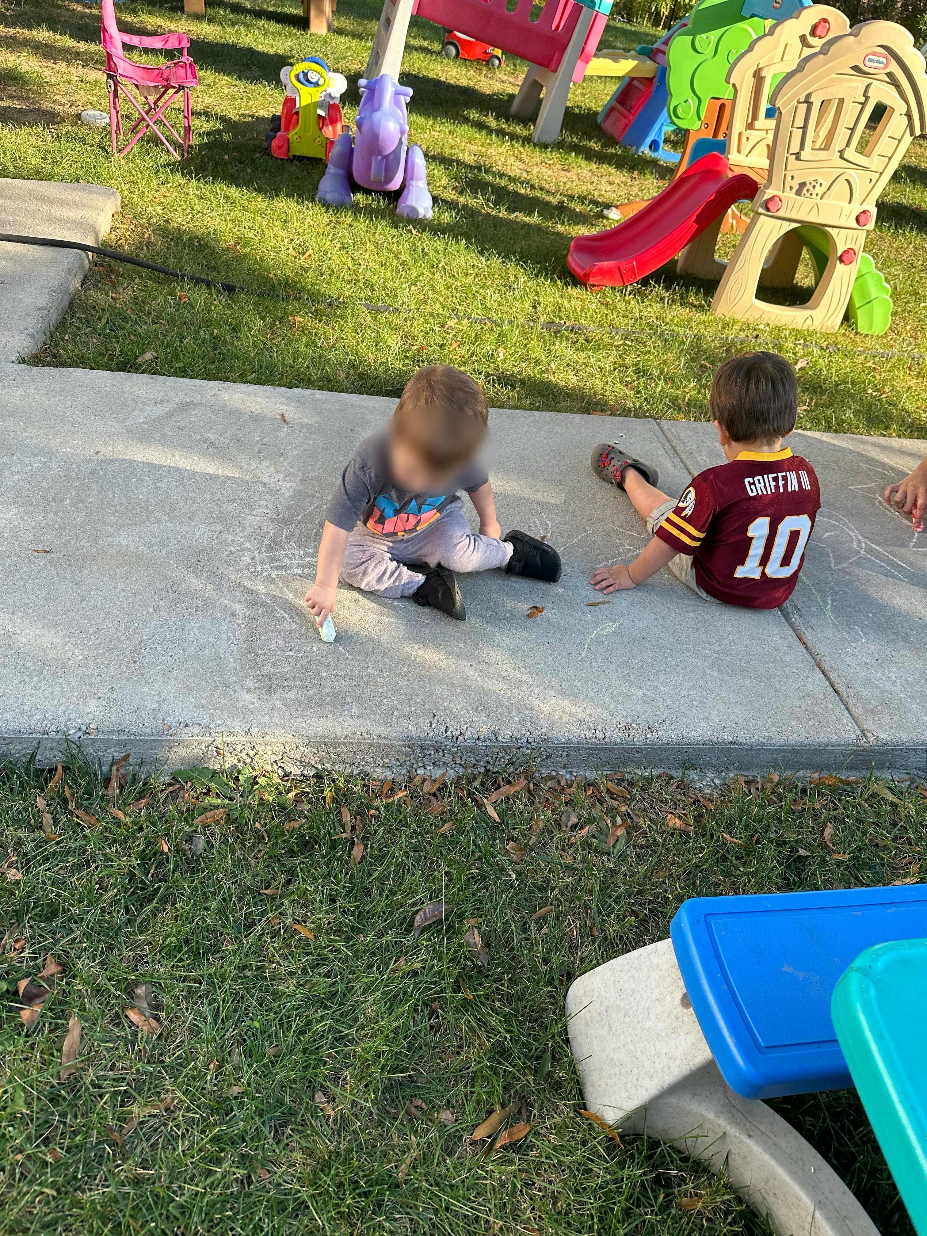 Two children sitting on concrete next to grass and playground equipment