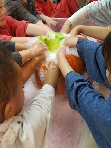 Multiple children's hands playing in soapy water with a green object