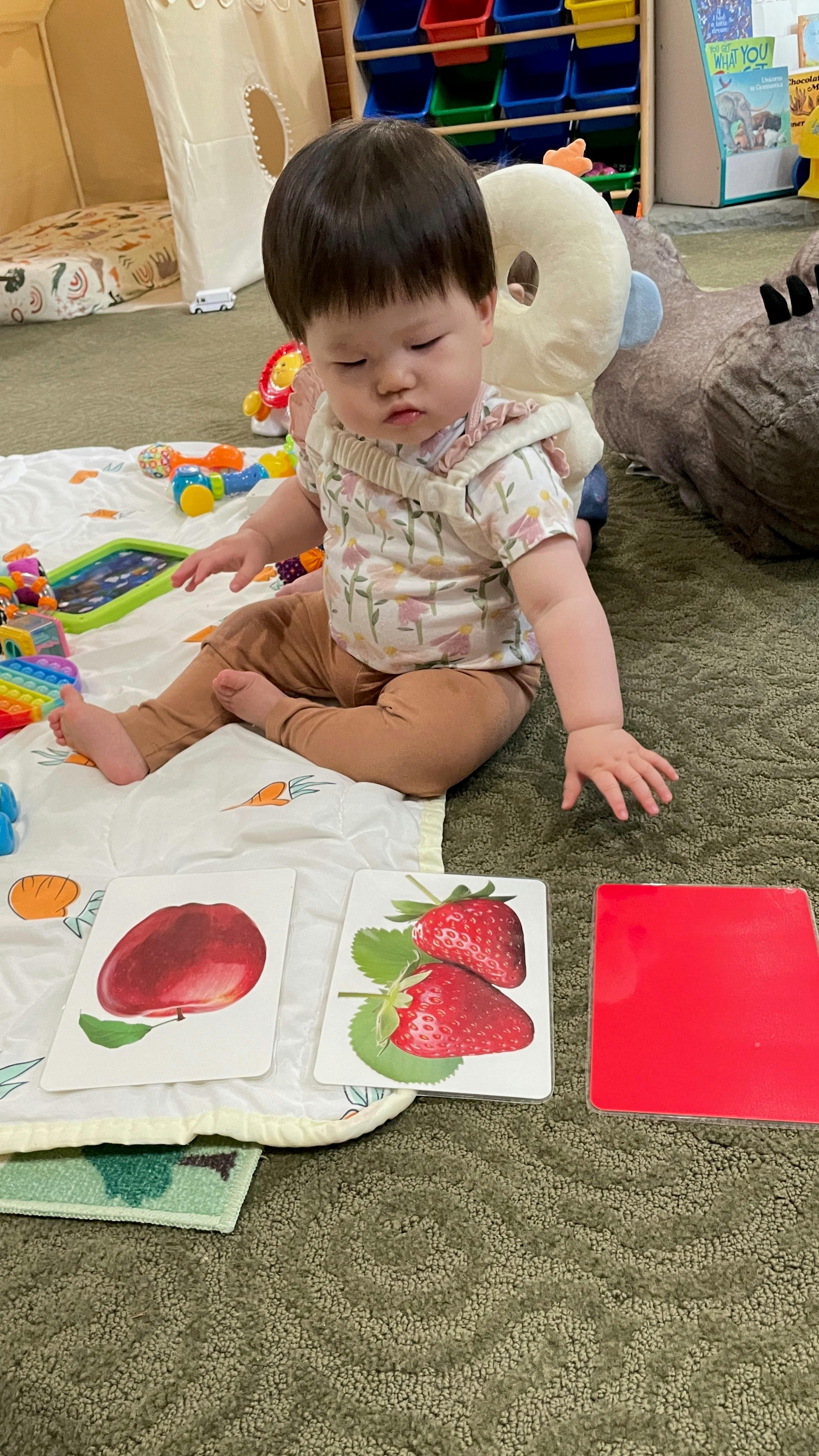 Child sitting on a mat with fruit flashcards