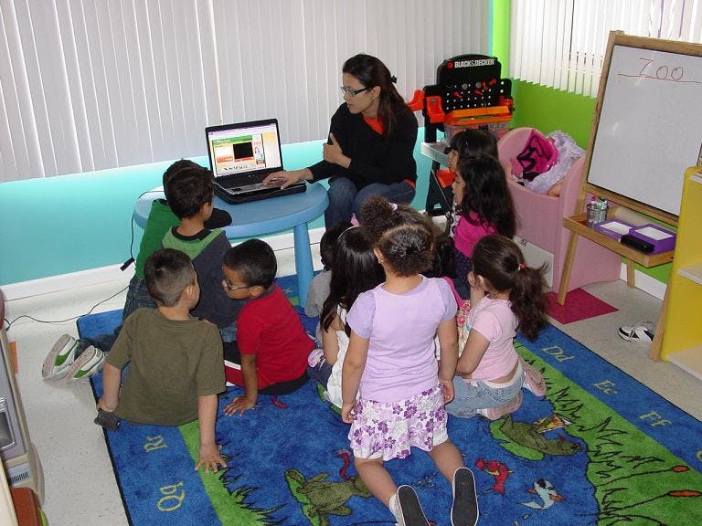 Person with children gathered around a laptop in a classroom