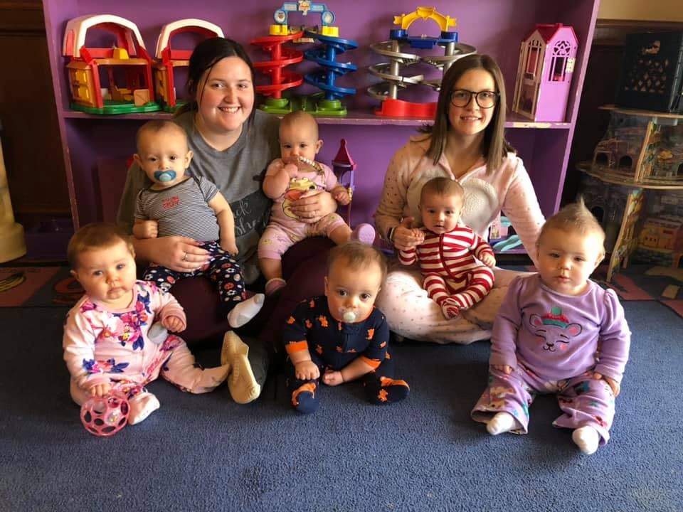 Two people sitting on the floor with multiple babies around them