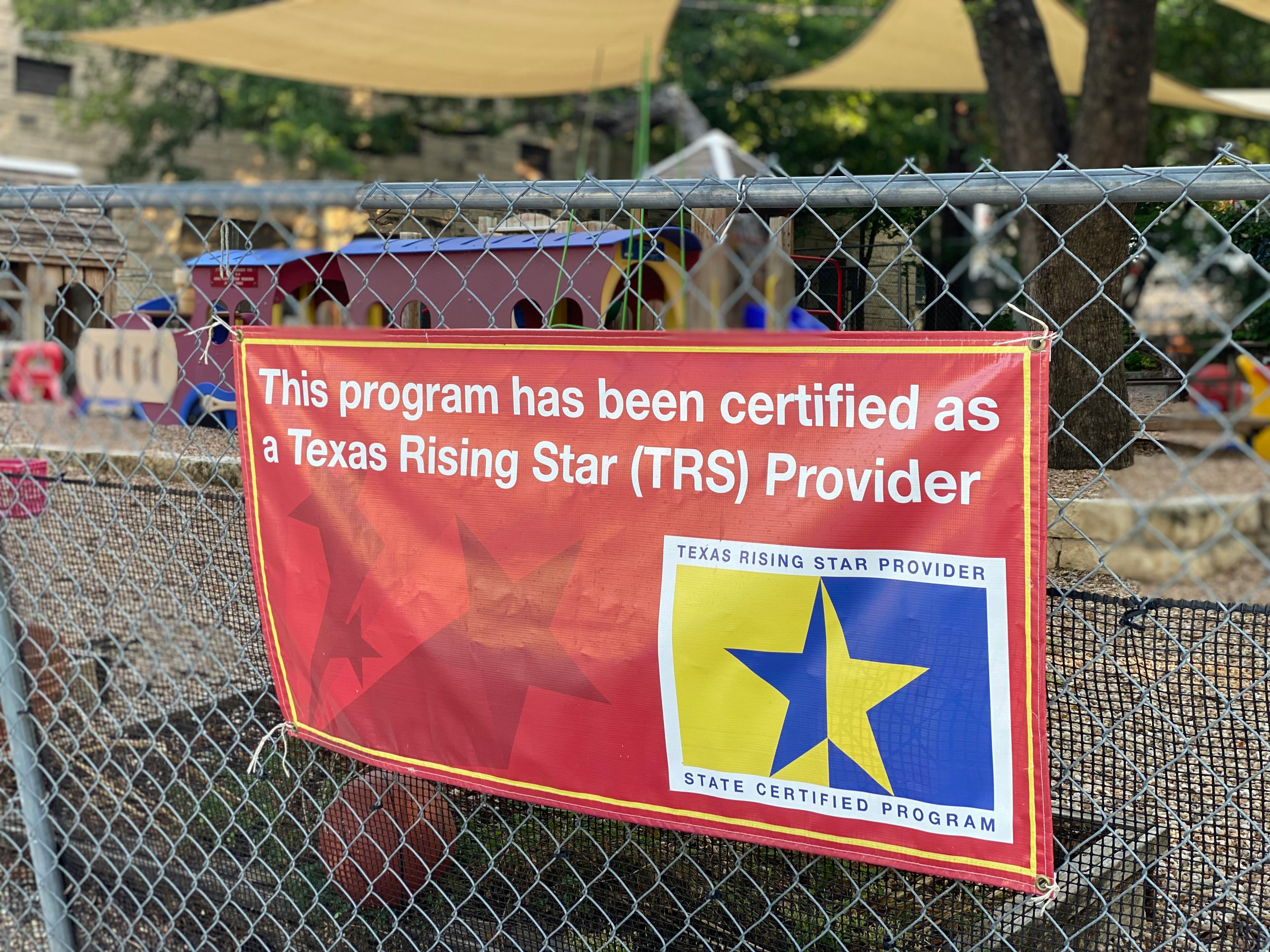 Red banner on a fence with text about Texas Rising Star Provider certification