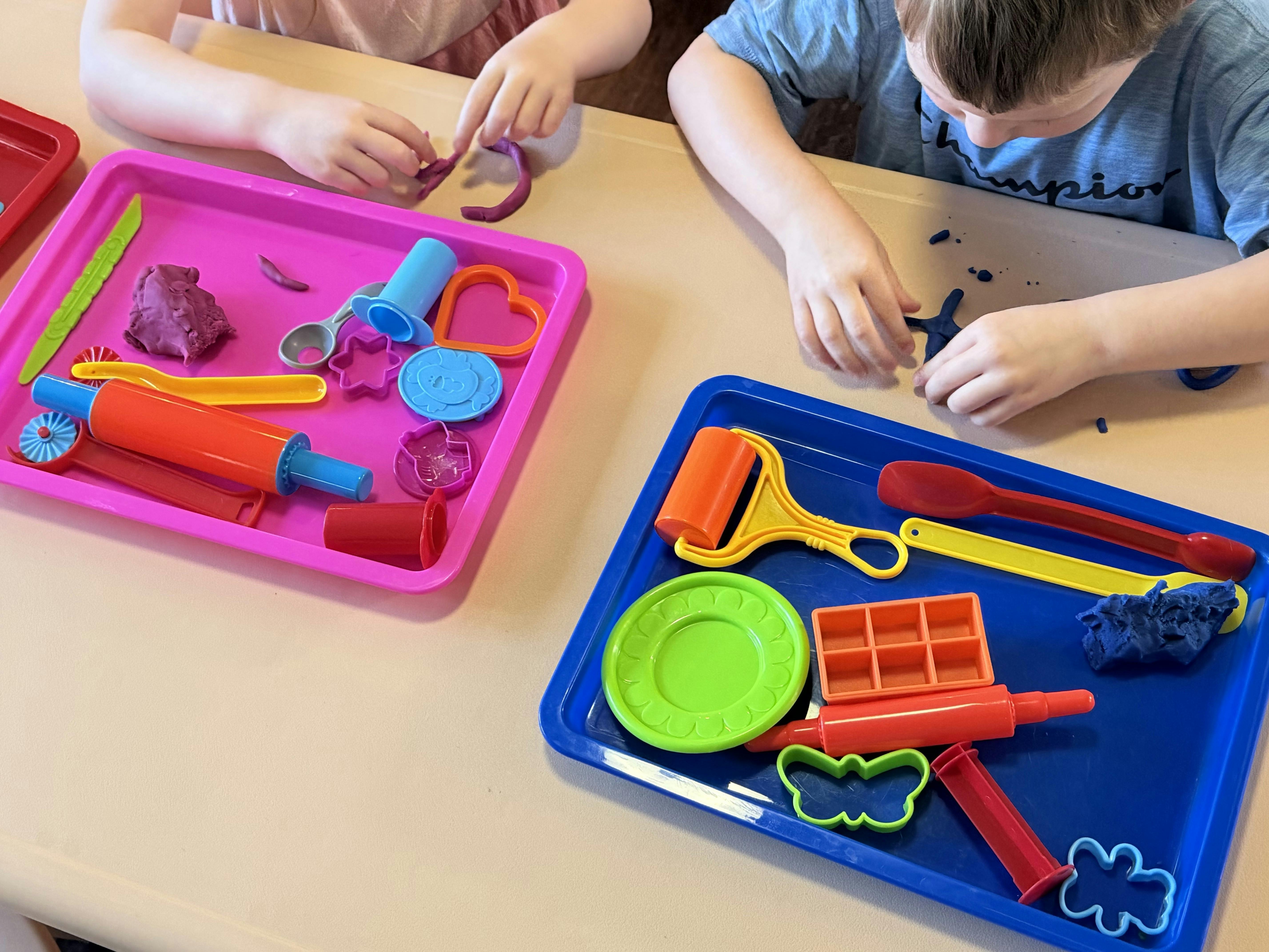 Two children playing with colorful modeling clay and plastic tools at a table