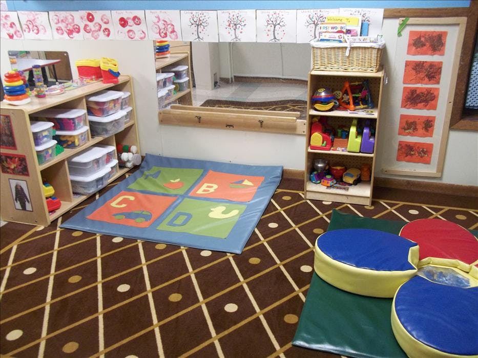 Classroom corner with shelves of toys, alphabet mat, and floor cushions