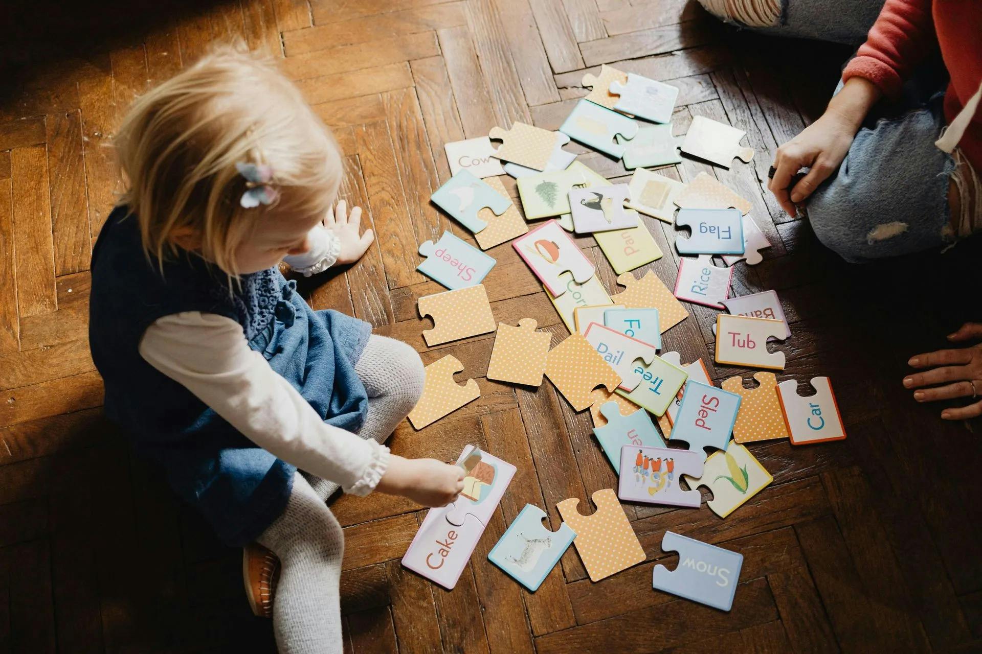 A child playing with matching word and picture puzzle pieces on a wooden floor
