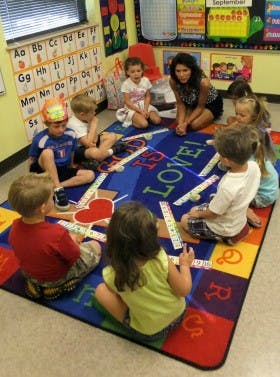 Adult and children sitting on a rug playing with letter tiles