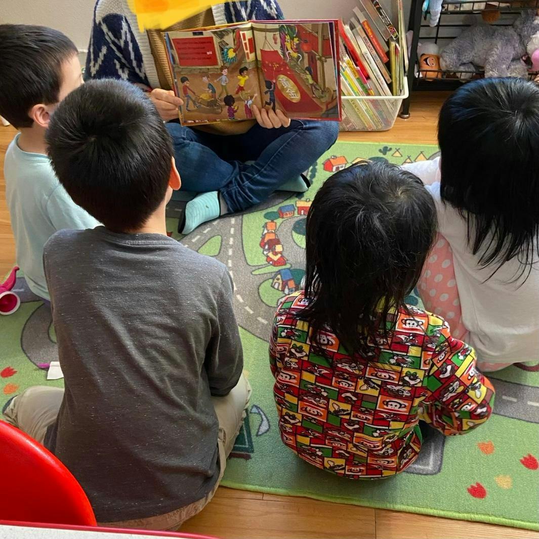 Person reading a book to three children sitting on a rug