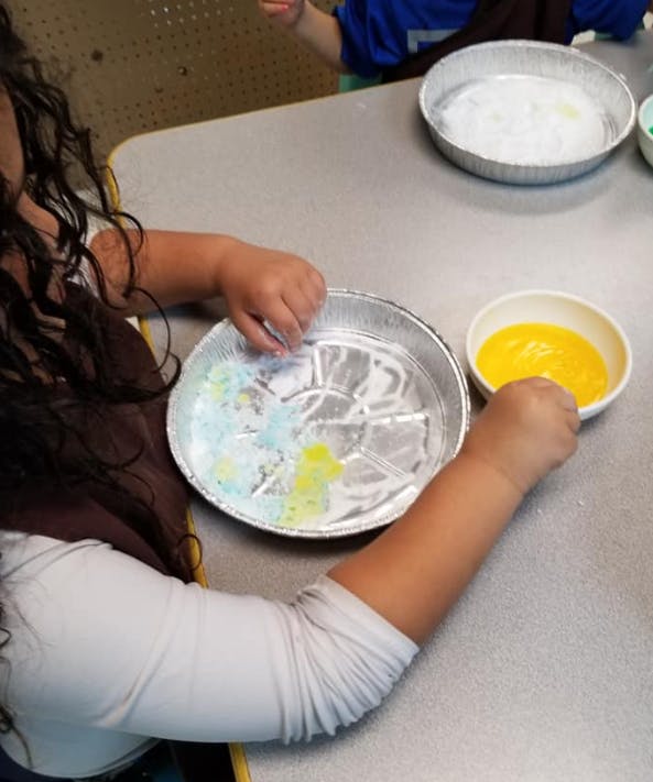 Child's hands mixing colors in a foil pan