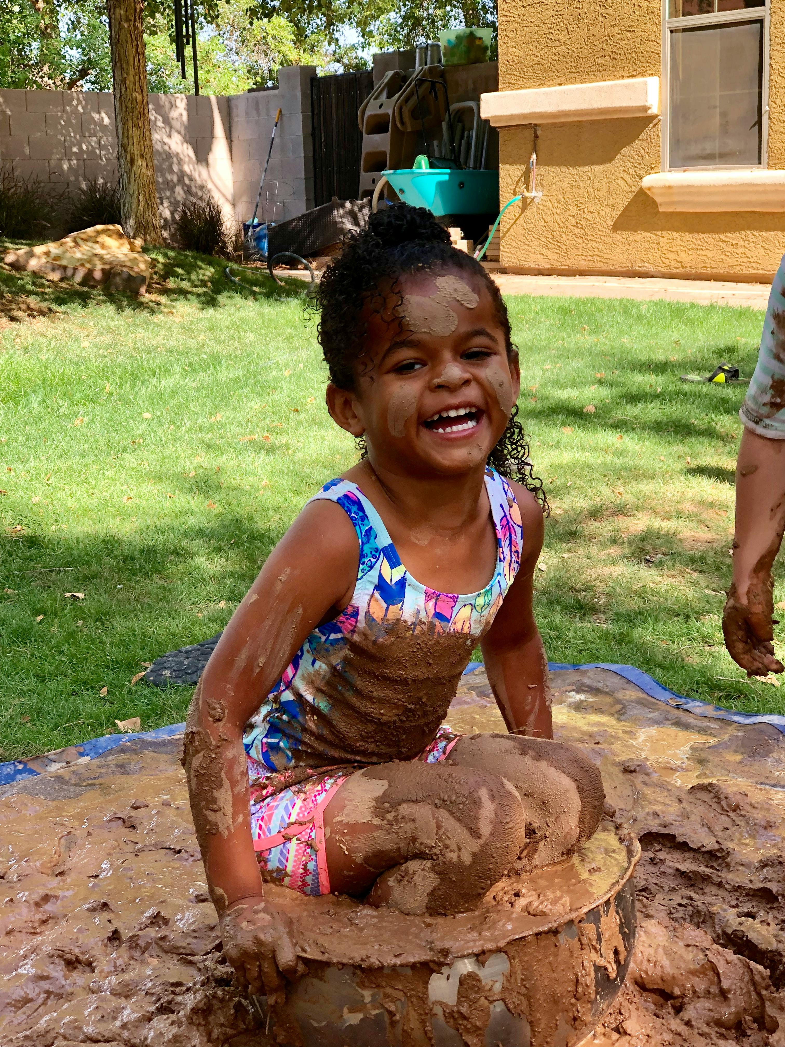 Child covered in mud sitting in a muddy puddle