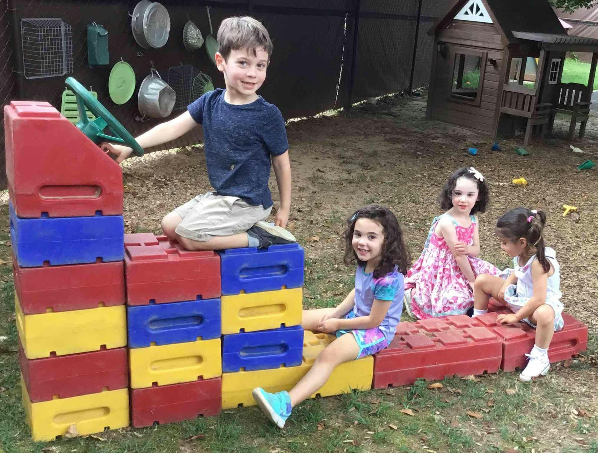 Child playing on colorful blocks with other children nearby