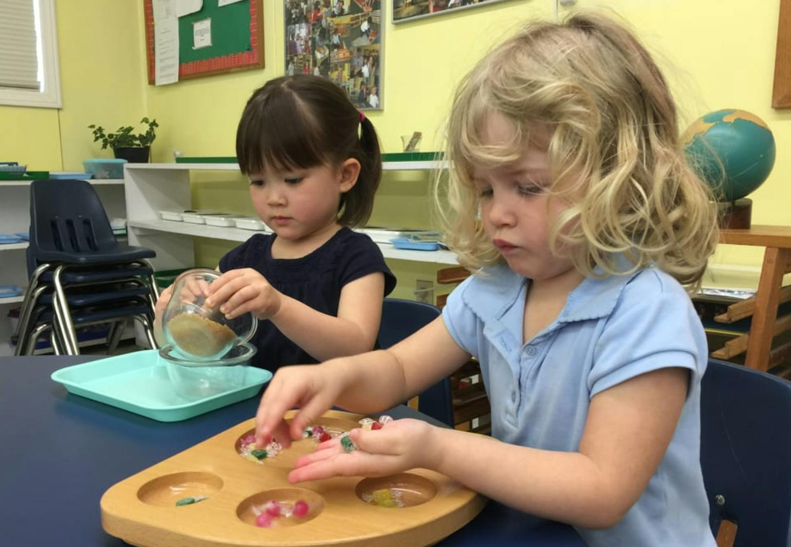 Two children playing with small objects at a table in a classroom