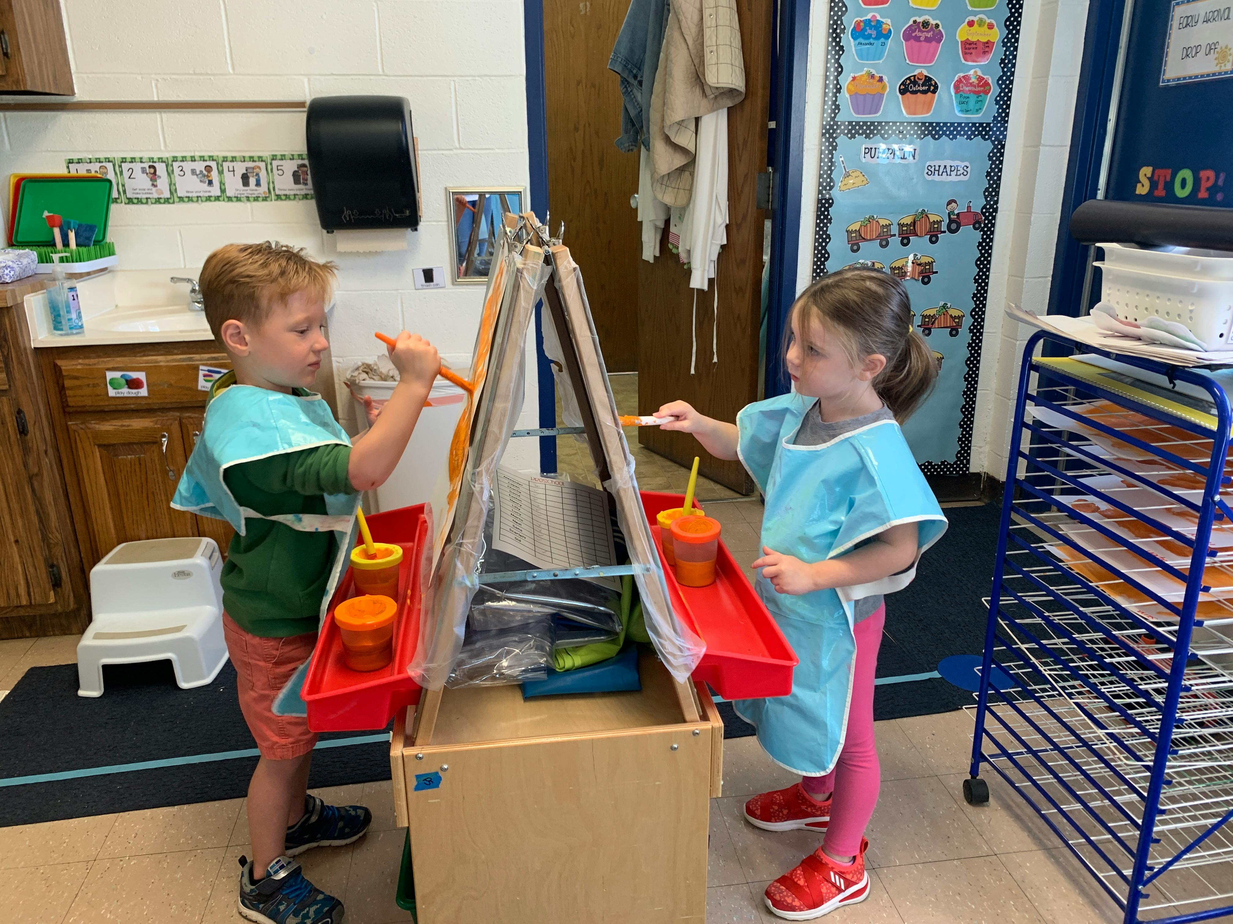 Two children painting at easels in a classroom