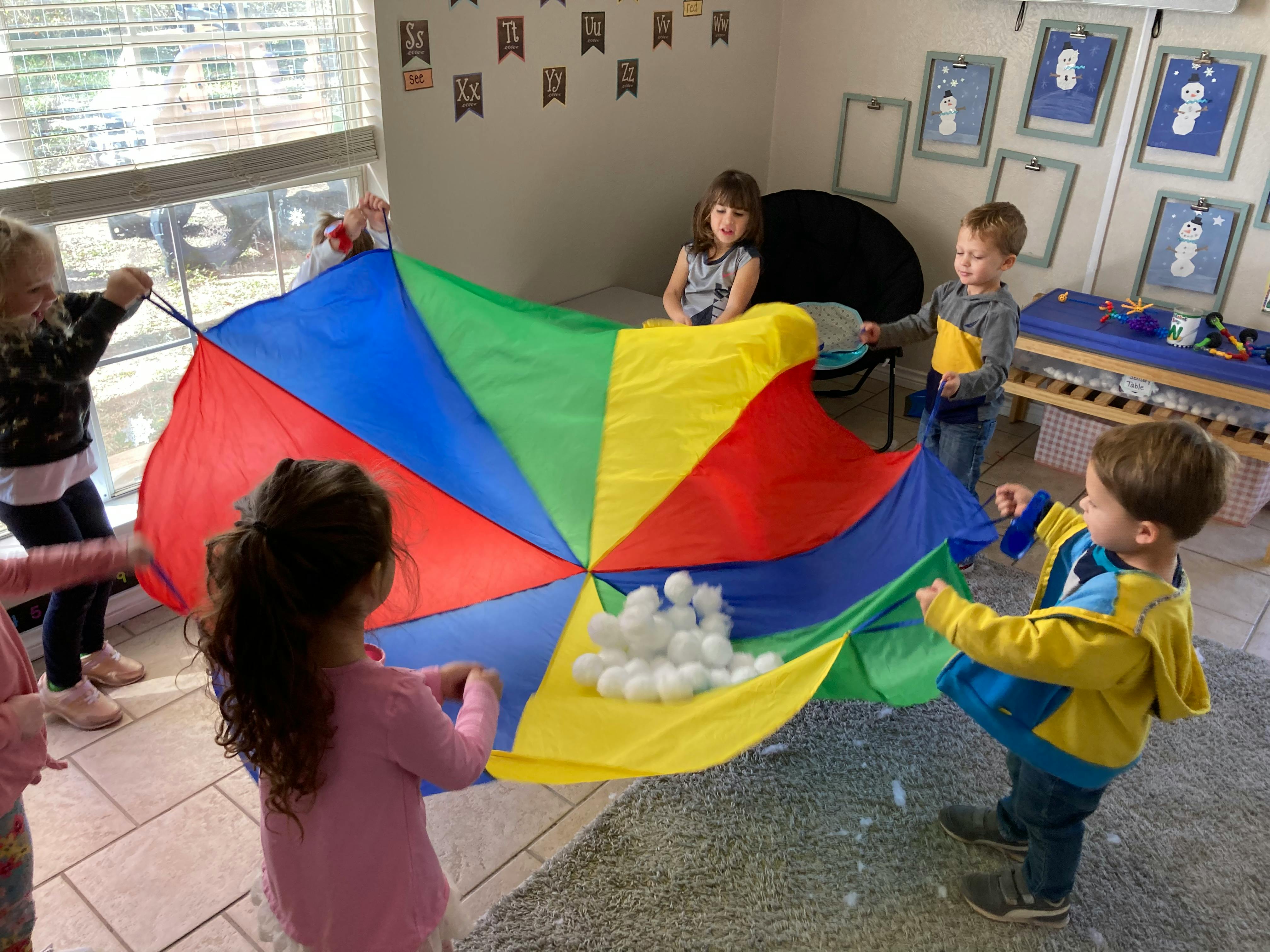 Children playing with a colorful parachute and white balls in a classroom
