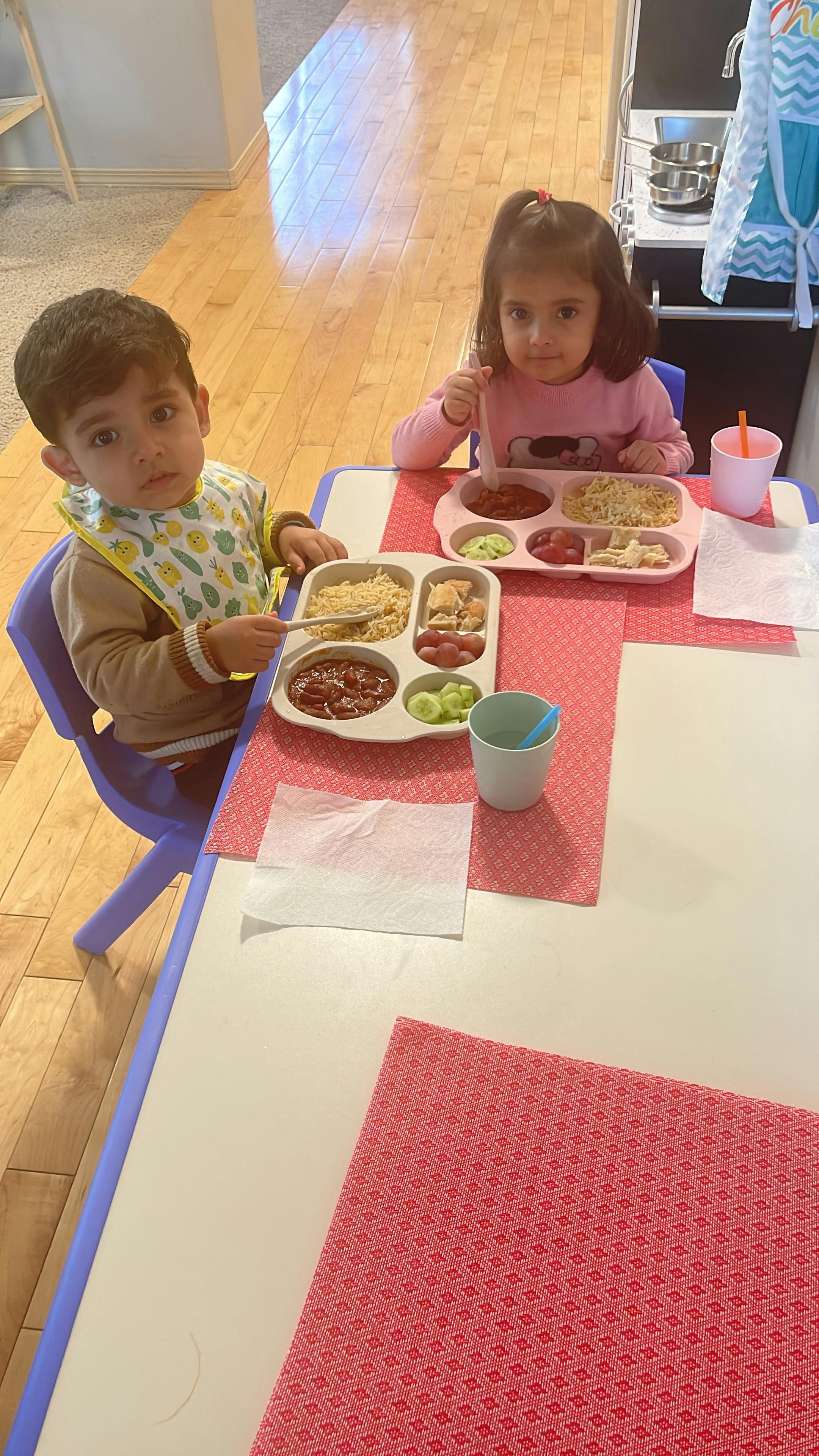 Two children sitting at a table with divided plates of food