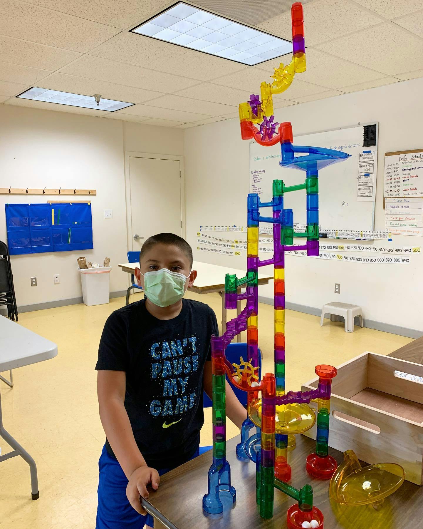 Child in a mask standing next to a tall, colorful marble run