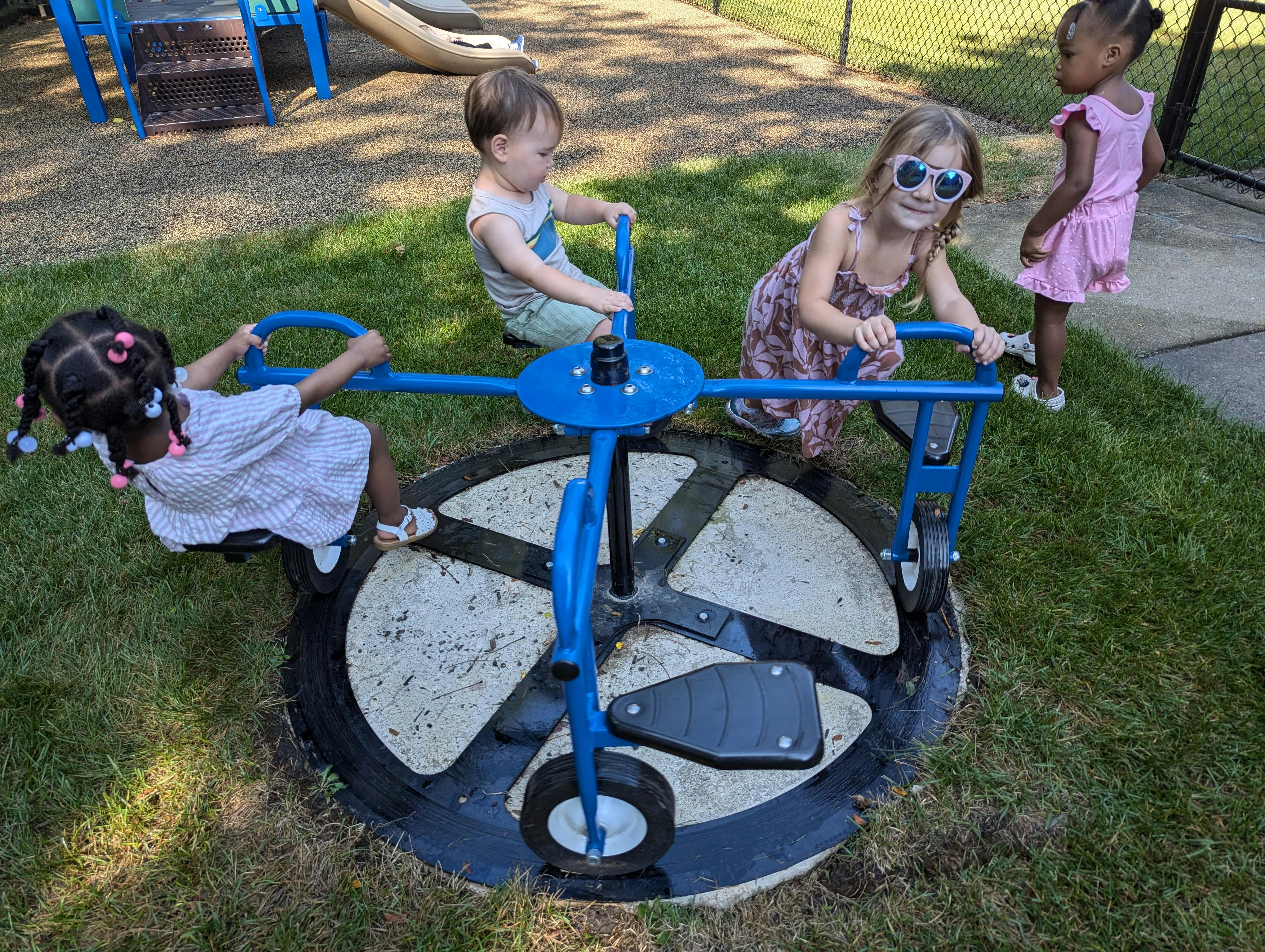 Three children playing on a blue merry-go-round in a grassy area