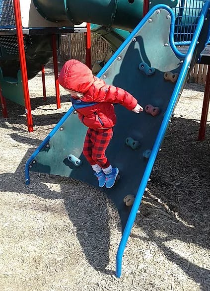Child in red jacket climbing a rock wall on a playground