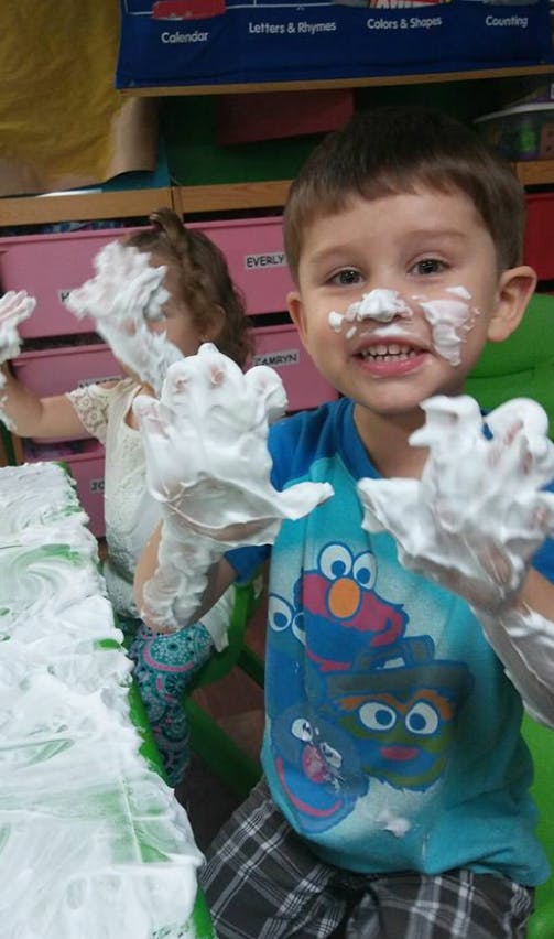 Child with shaving cream on face and hands, another child in background